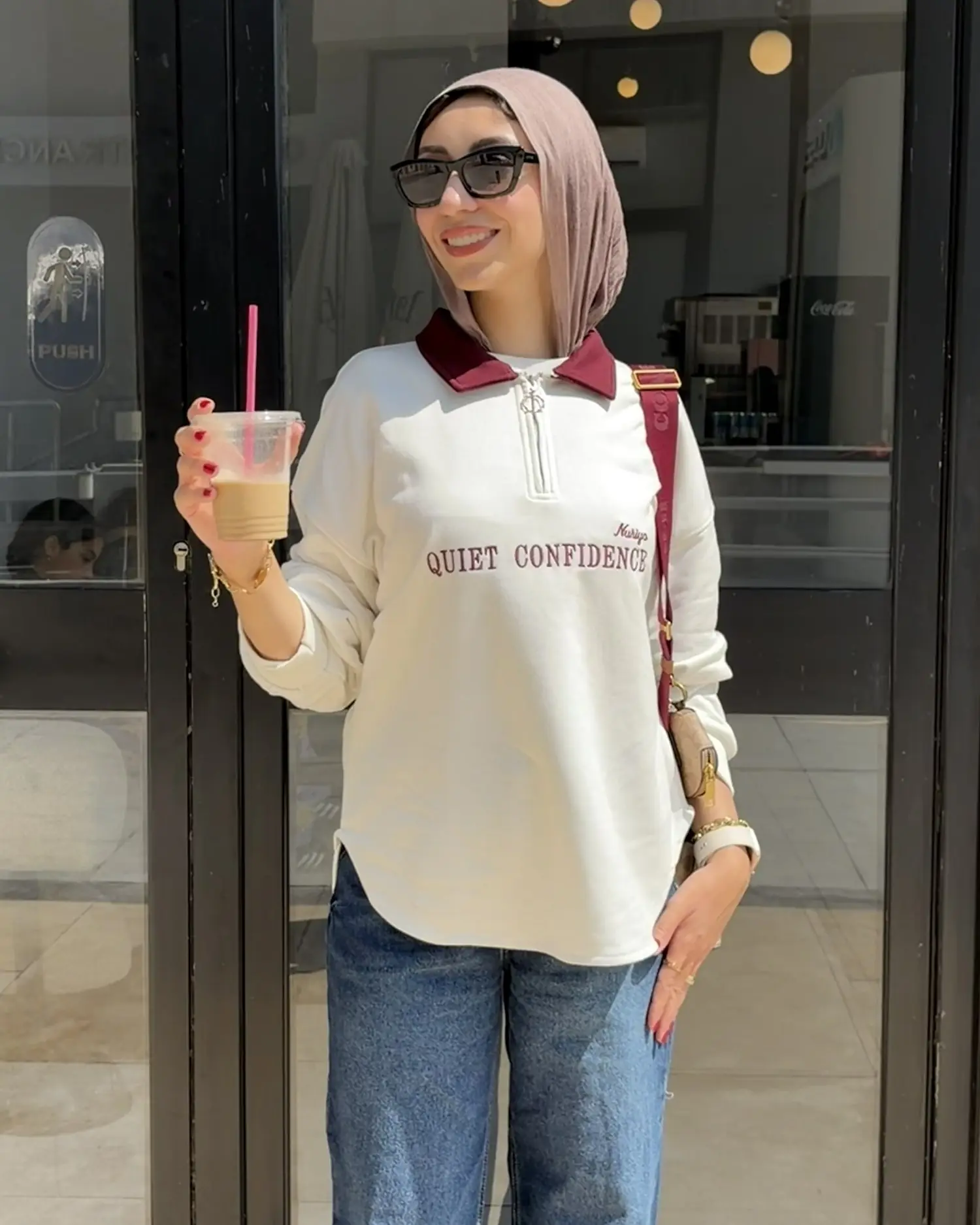 Smiling girl in the white Quiet Confidence quarter-zip with a burgundy collar, wide-leg jeans and an iced coffee